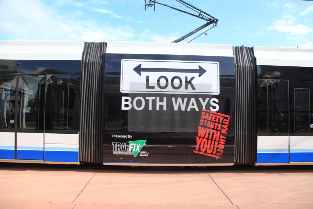 A photographic image of safety warnings advertised on the side of a light rail train.