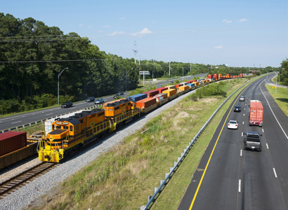 A photographic image of a freight train running between two parallel highways.