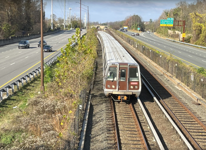 A photographic image of a passenger train moving between two parallel highways.