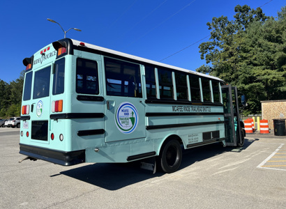 Photographic image of a parked teal bus with a clear blue sky in the background.