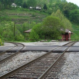 A photographic image of two railroad tracks at a street crossing in a rural setting.