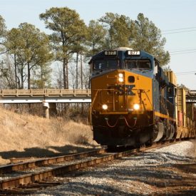 A photographic image of an incoming freight train traveling along railroad tracks.