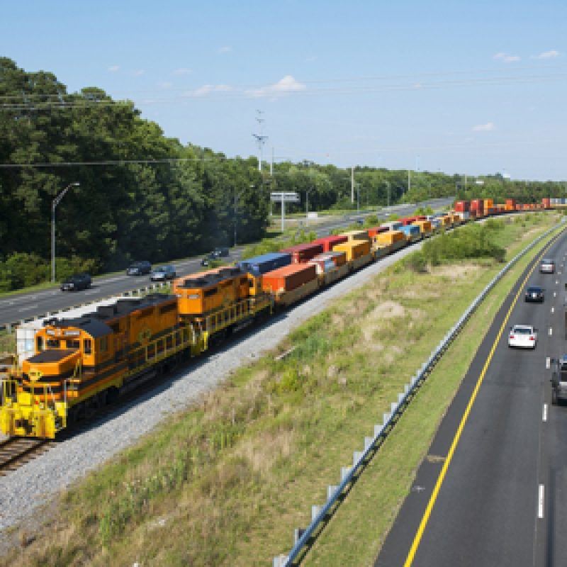 A photographic image of a freight train running between two parallel highways.