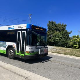 A photographic image of a white bus with blue and green accents traveling down a rural street.